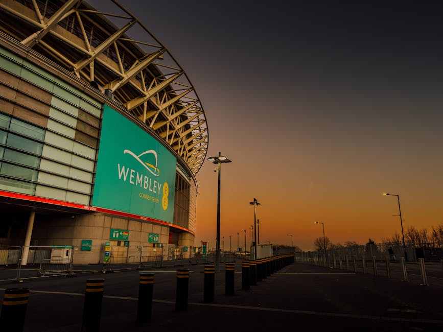 A row of empty red plastic stadium seats with attached armrests, aligned along a concrete walkway inside Twickenham Stadium. The seats are clean and glossy, with some showing slight reflections from t